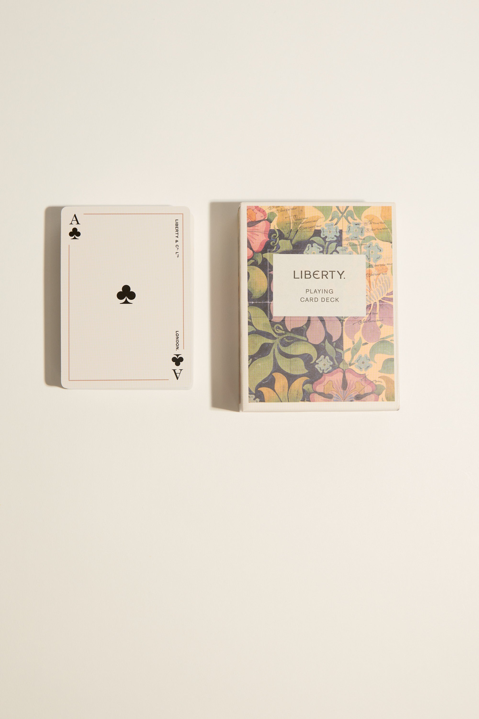 An ace of clubs playing card rests beside a colorful floral box labeled "Liberty Archive Playing Card Deck" by Other, displaying British-inspired design on a light surface.