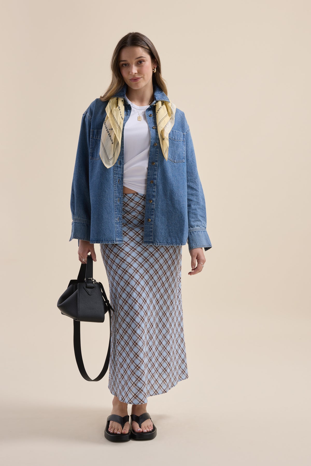 Woman in denim jacket, white top, Max The Perfect Slip Skirt, scarf, black bag, and sandals.