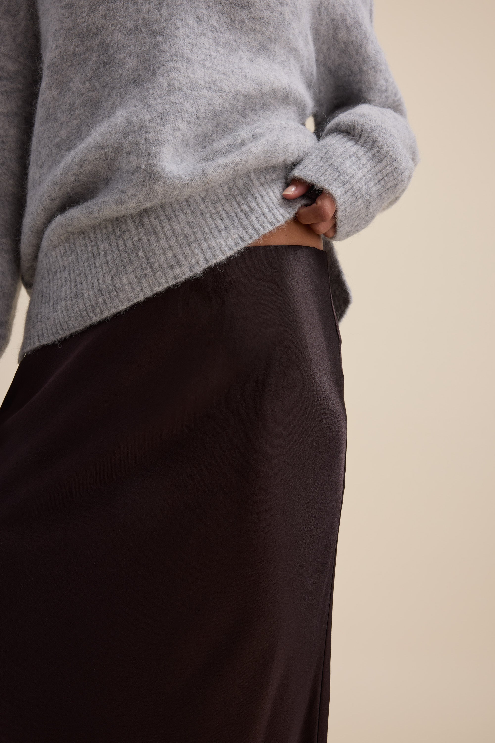 Person in a gray sweater and Max's The Perfect Slip Skirt in dark brown satin, holding up the sweater.