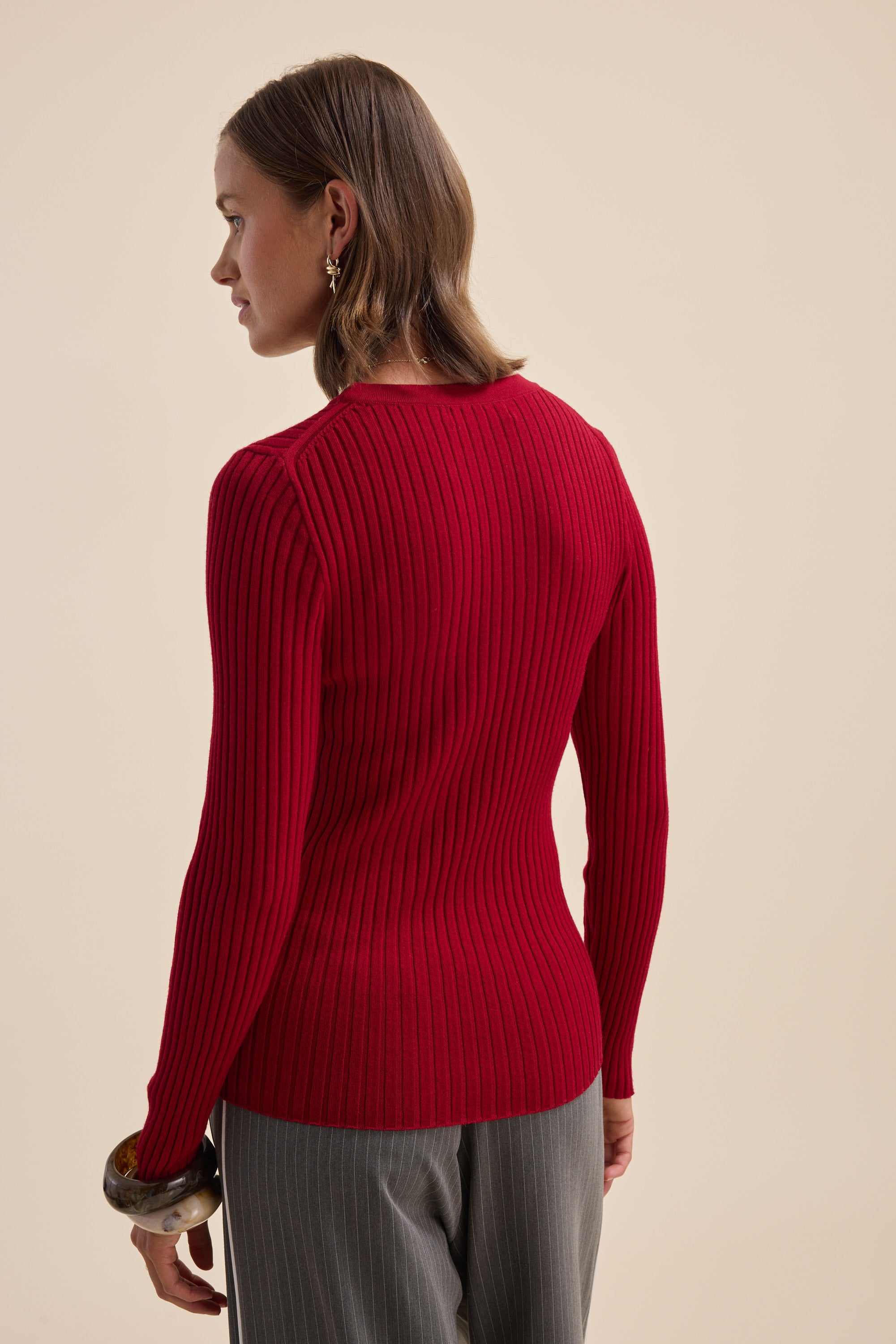 A woman wears the Elementary ZQ Merino Crew Neck Top in red with gray pants, facing away.