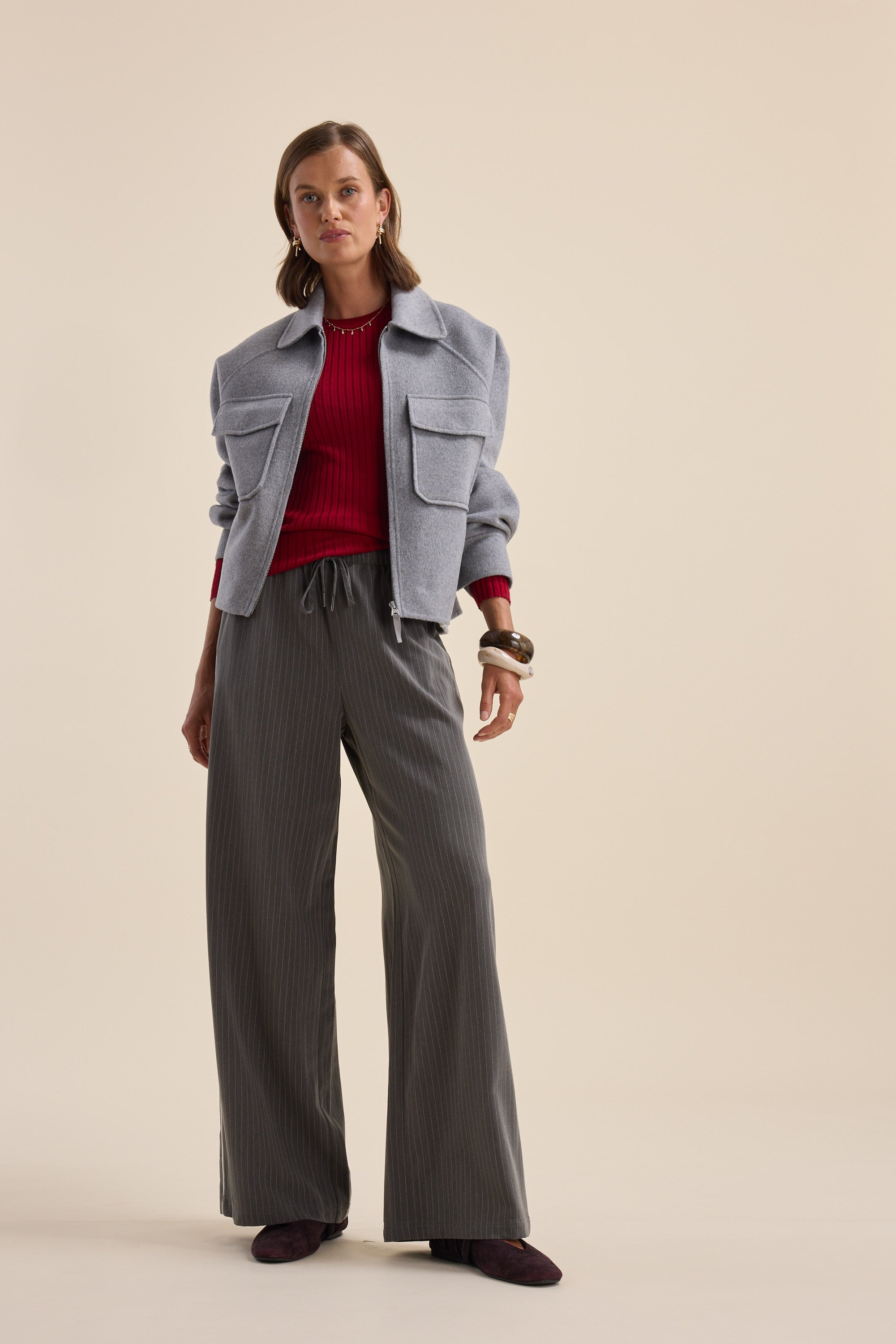 Woman in gray jacket, Elementary ZQ Merino Crew Neck Top, pinstripe pants, and burgundy shoes.