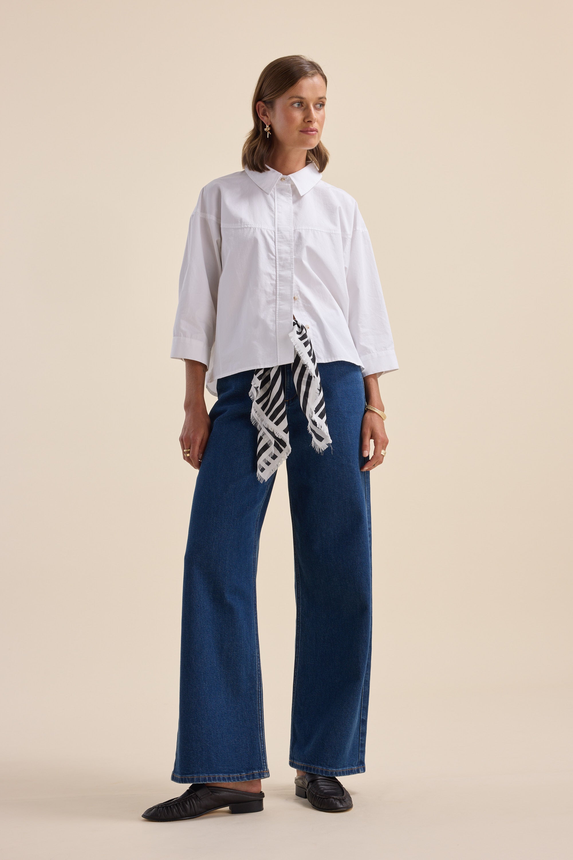 Woman wears Elementary Yoke Detail Shirt and wide-leg blue jeans against a beige background.