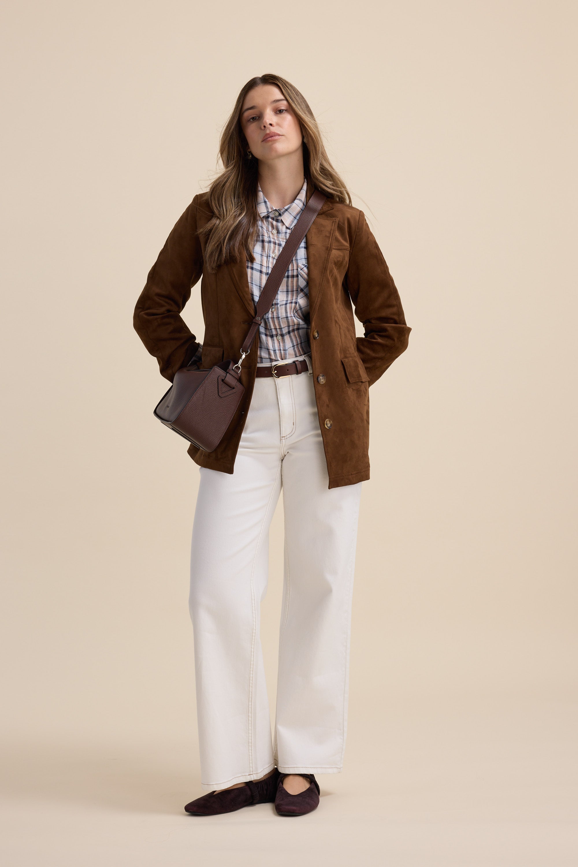 Woman stands confidently in an Elementary Oversized Shirt, brown blazer, and white pants.
