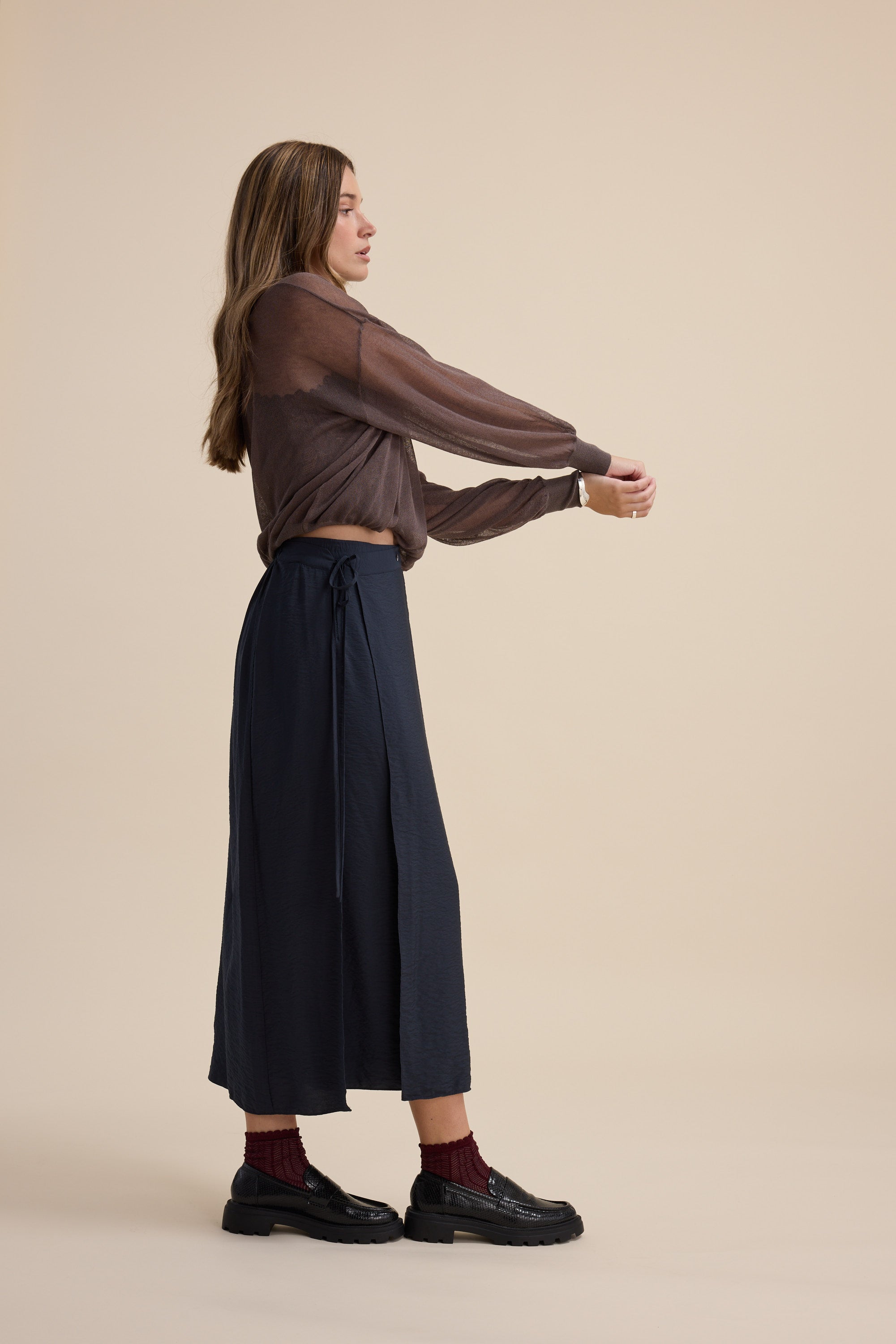 Woman in a sheer brown top and Elementary Wrap Detail Skirt by Elementary stretches sideways.