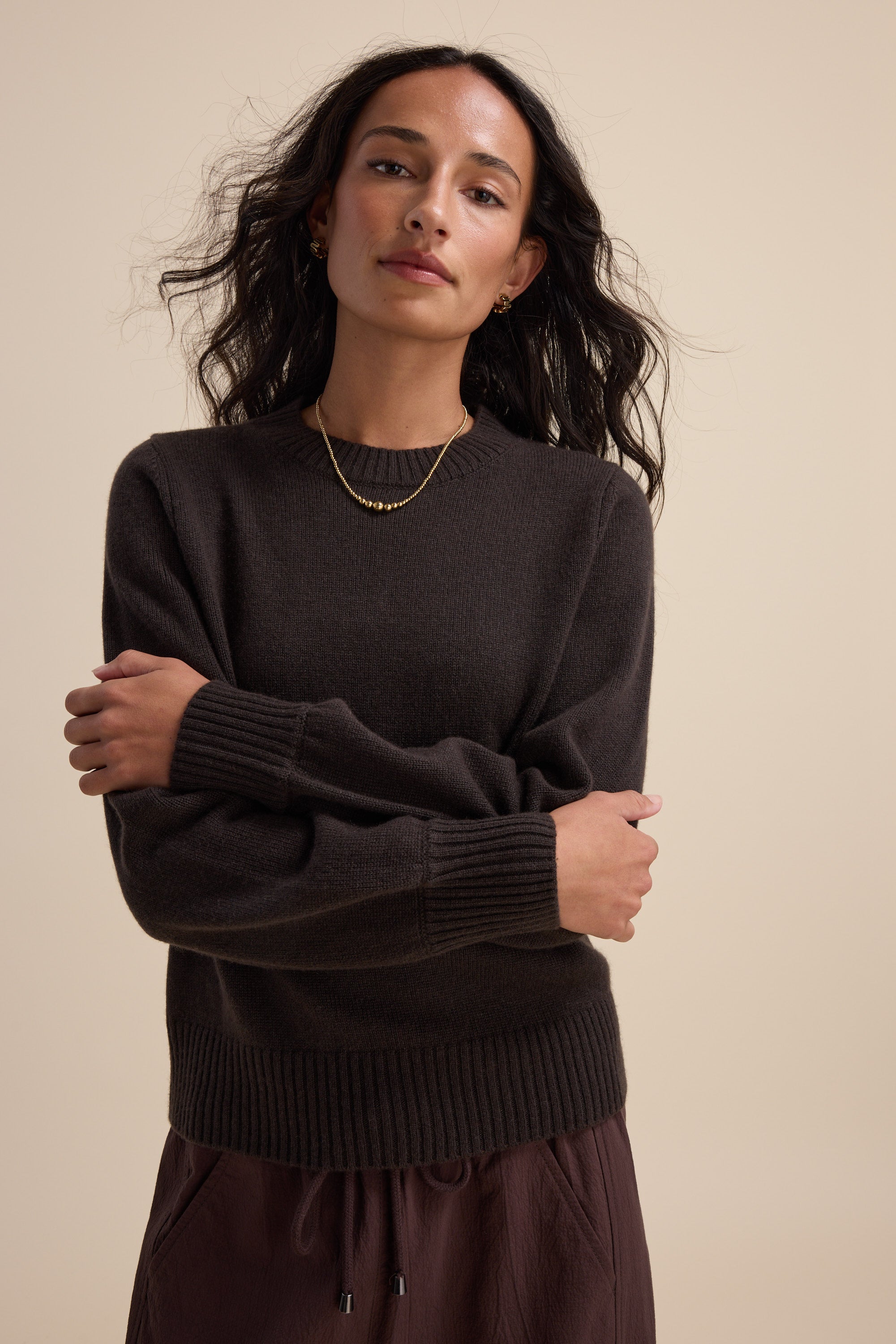 Woman in Elementary Cashmere Blend Crew Neck Sweater by Elementary, arms crossed, beige background.