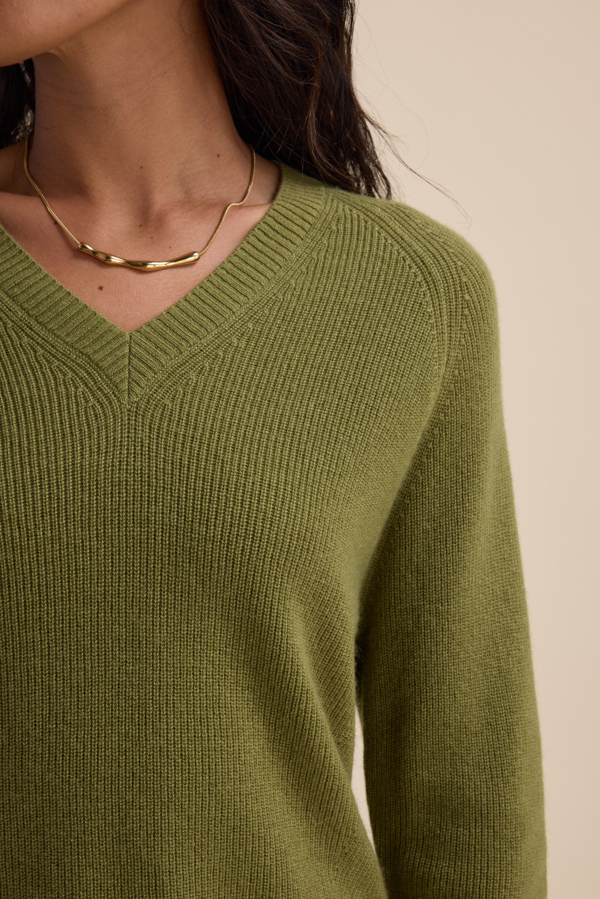 Person wearing an Elementary Cashmere Blend V Neck Sweater in olive green and a gold necklace.