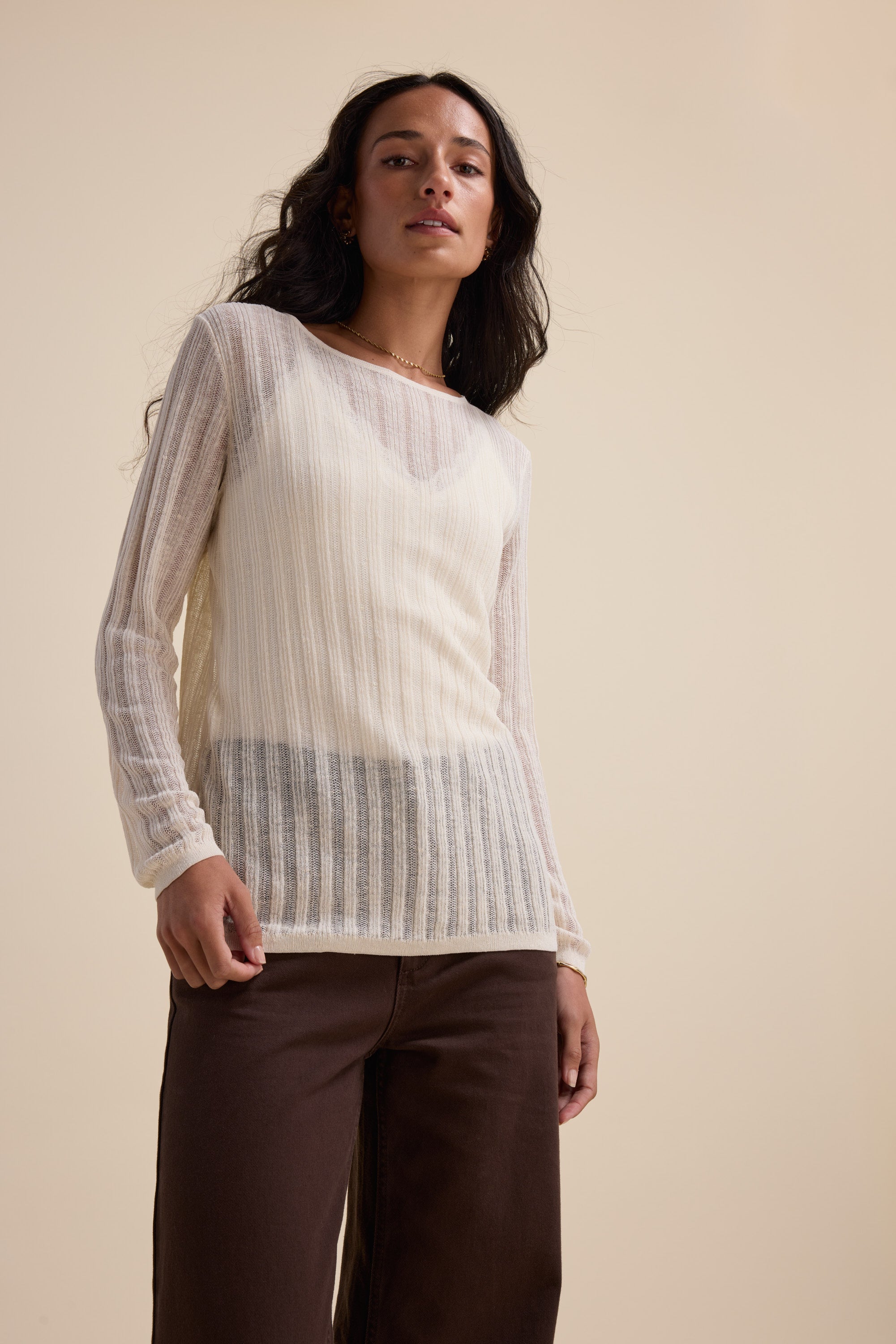 Woman in Elementary's cream Knitted Layering Top and brown pants against a beige background.