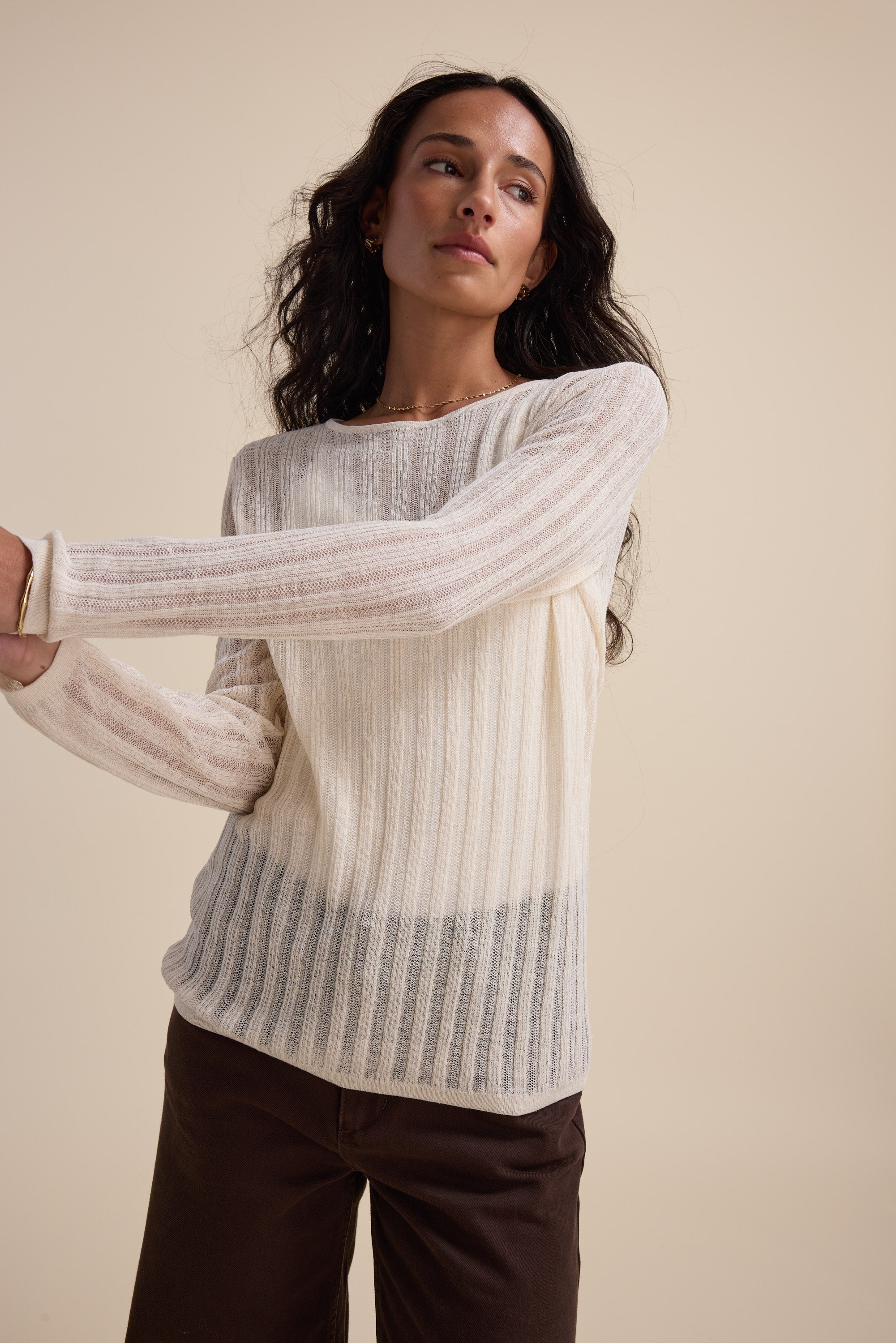Woman wears the Elementary Knitted Layering Top in ivory with brown pants against a beige backdrop.