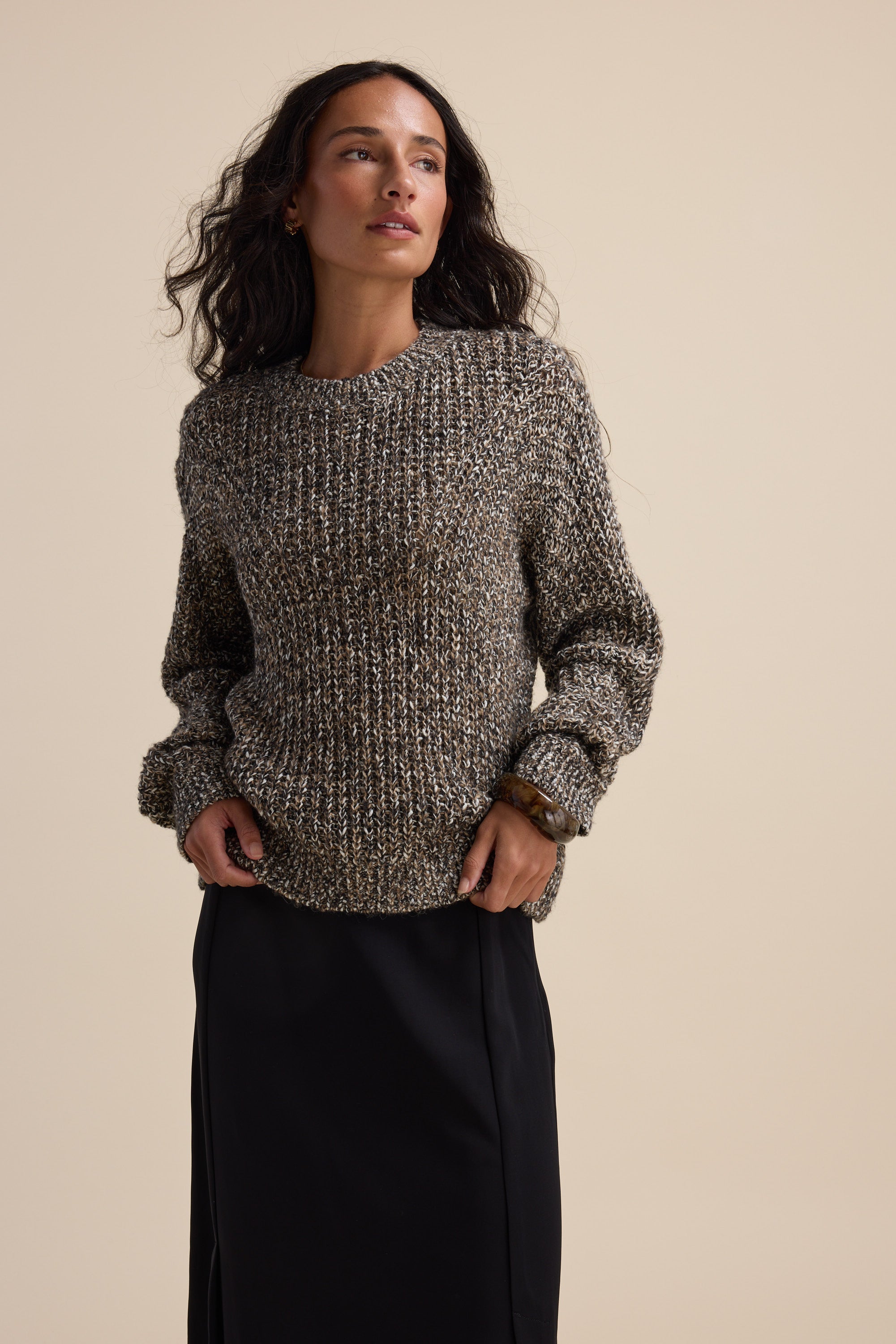 Woman in an Elementary Chunky Knit Sweater and black skirt against a beige background.