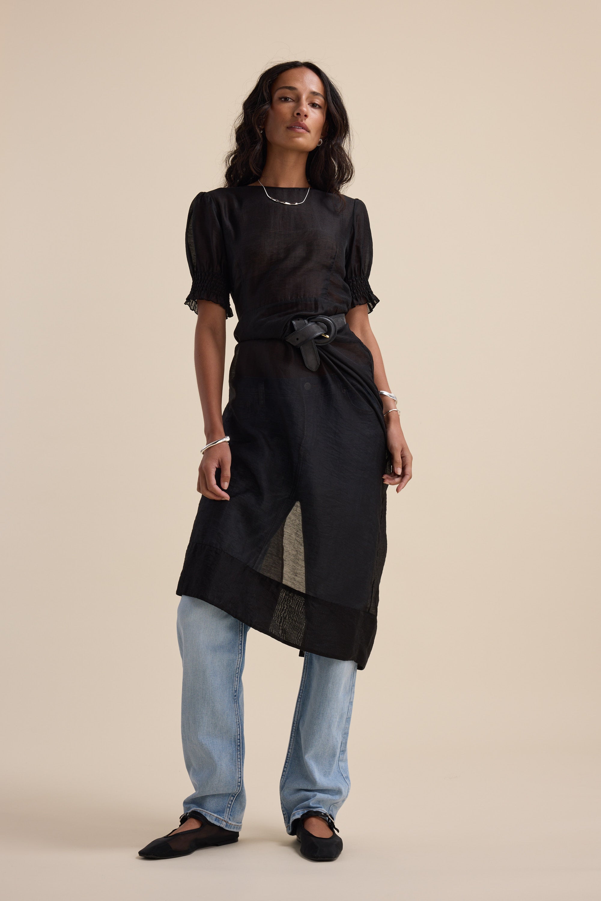 Woman in The Sheer Layering Dress by Max over light blue jeans and black flats, beige background.