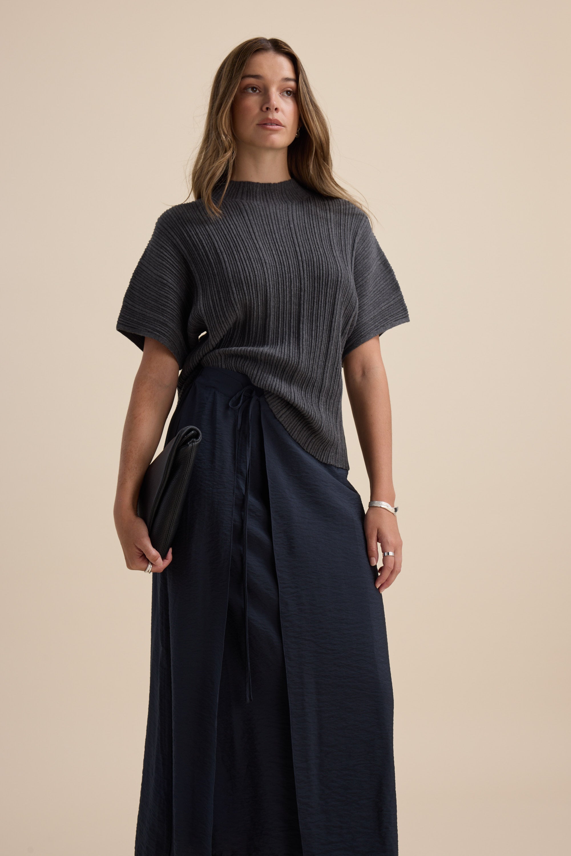 Woman in gray ribbed top and Elementary navy wrap midi skirt with adjustable waistband, holding clutch.