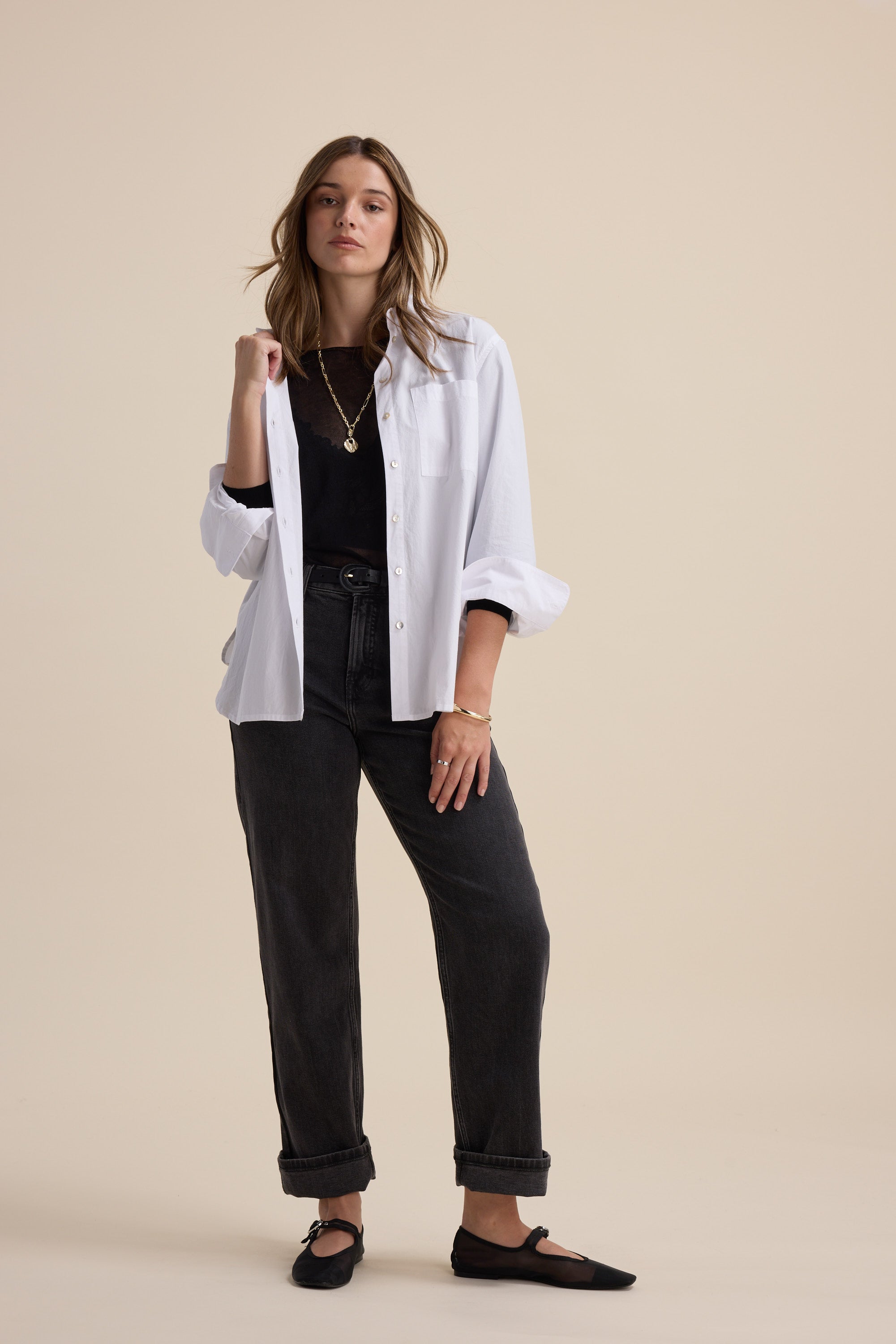 Woman wears Max Addie Sheer Knitted Top, white shirt, dark jeans, black shoes, beige background.