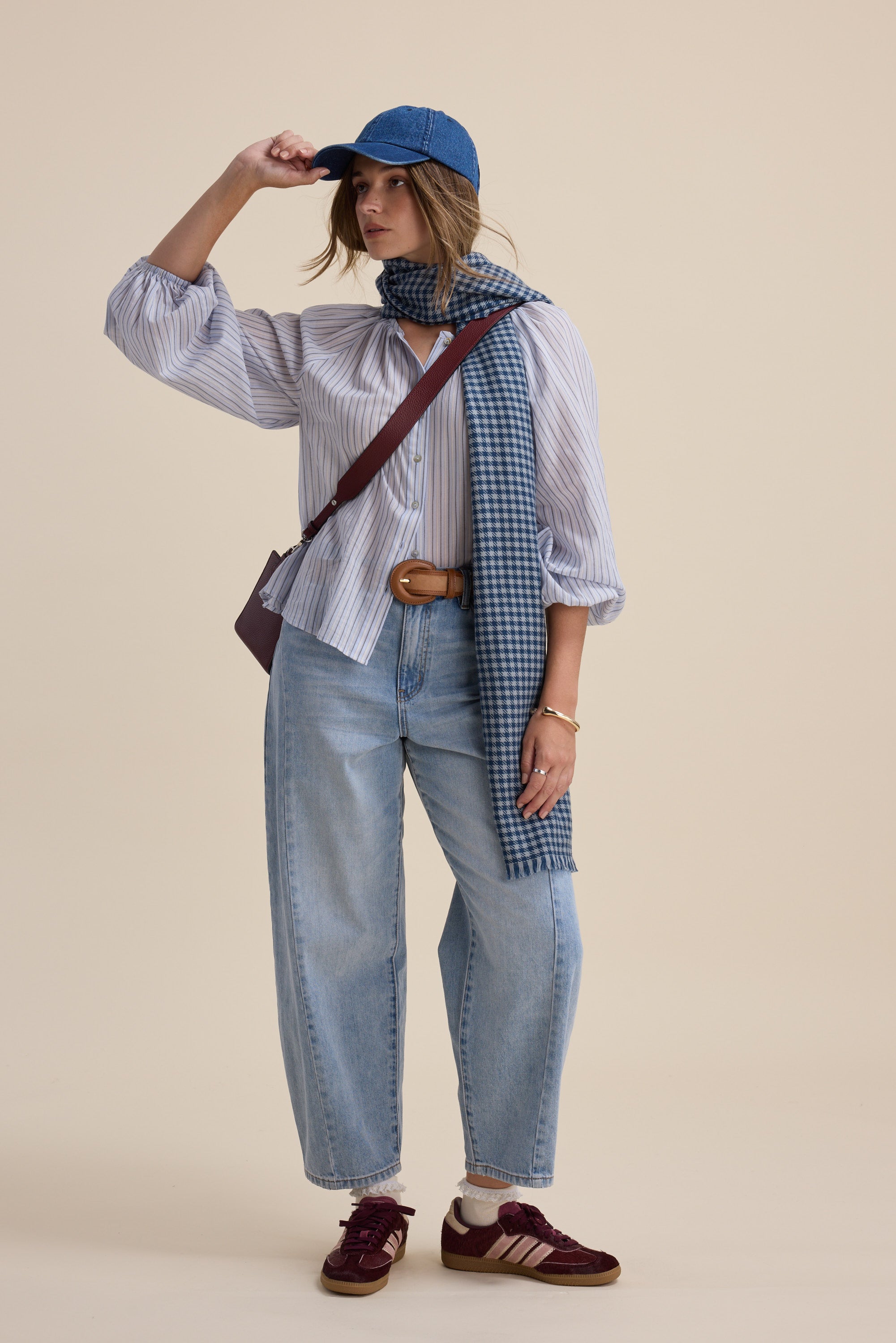 Person in Vivian Button Front Blouse by Max, striped shirt, jeans, scarf, cap, maroon shoes.