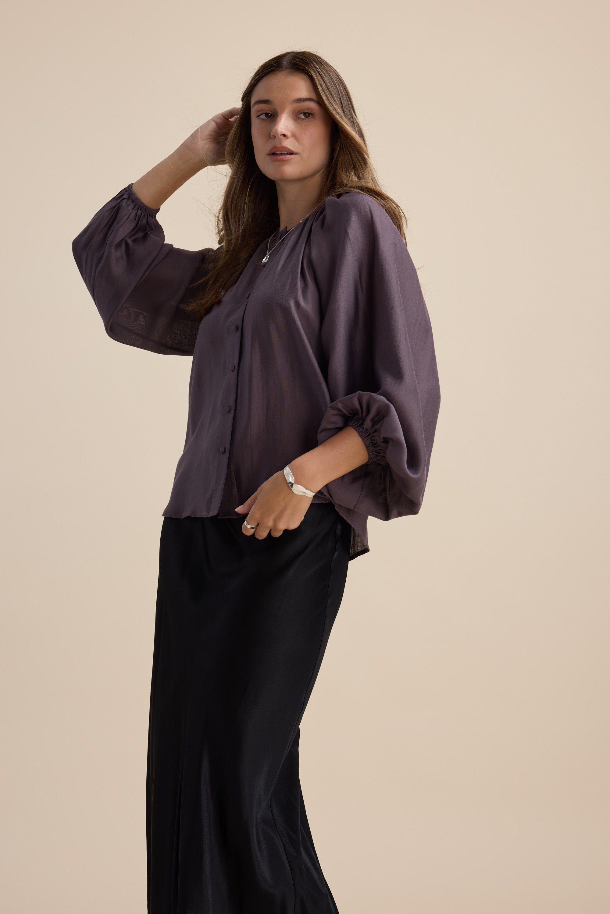 Woman in Max Vivian Button Front Blouse, purple, with a black skirt on a beige background.