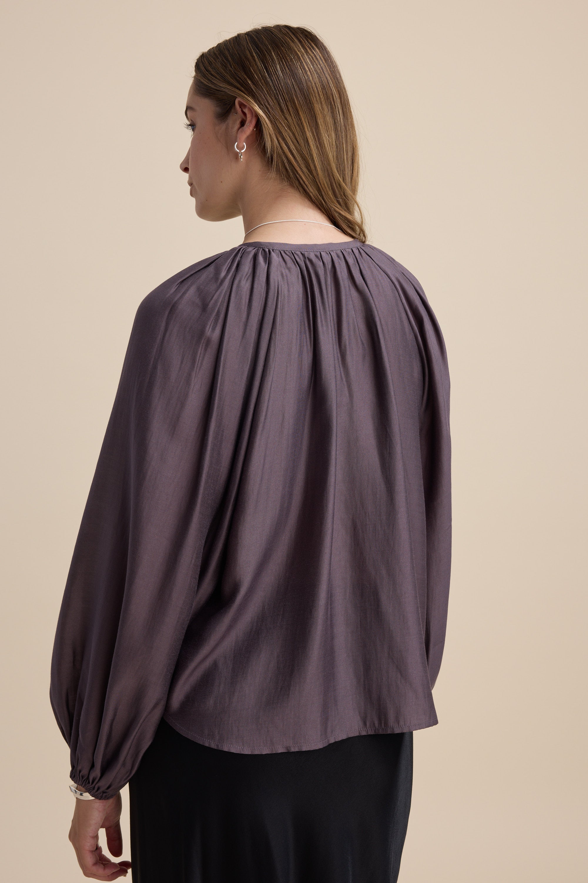 Woman in the Max Vivian Button Front Blouse facing away against a beige background.