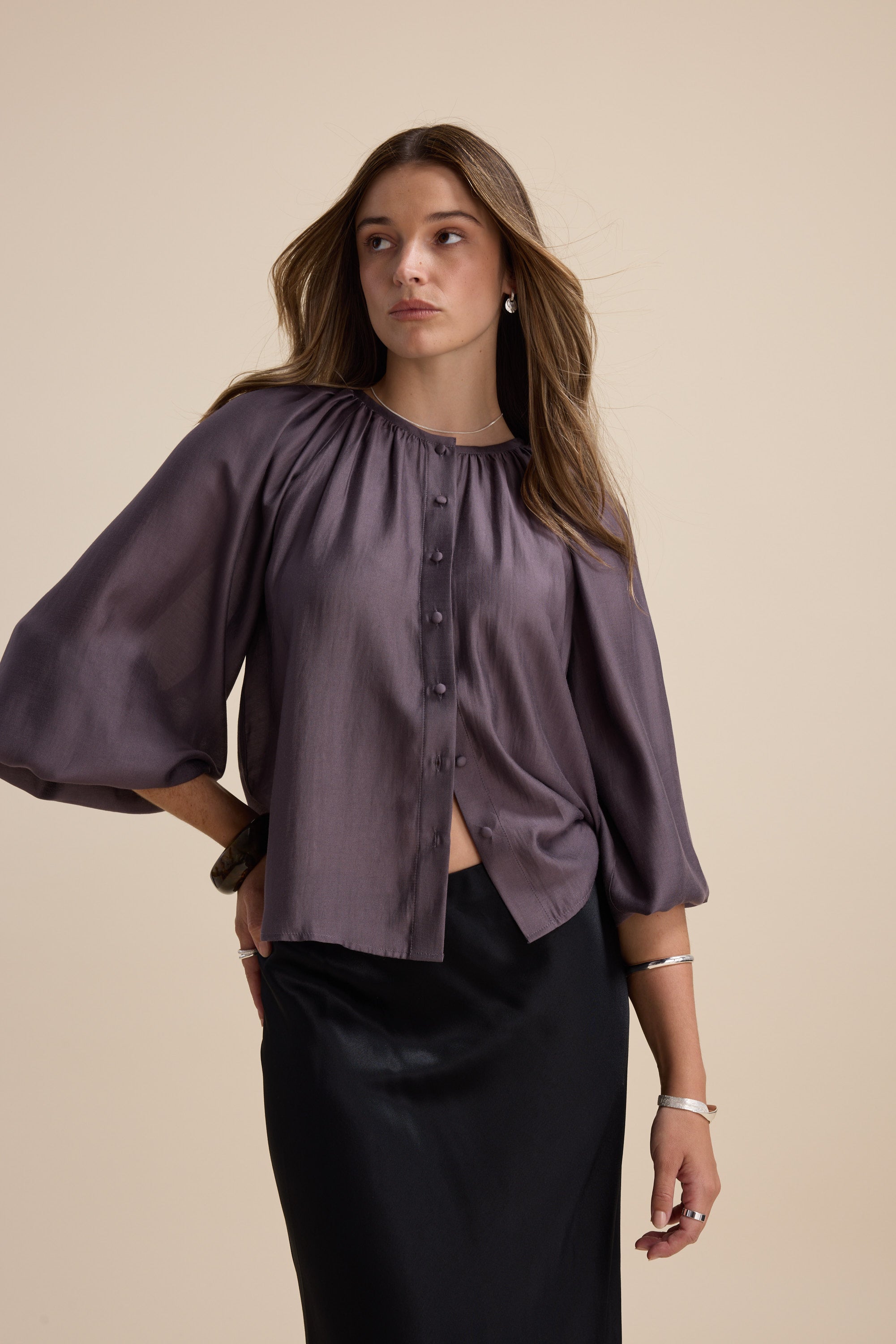 Woman in Max Vivian Button Front Blouse with blouson sleeves and black skirt on beige background.