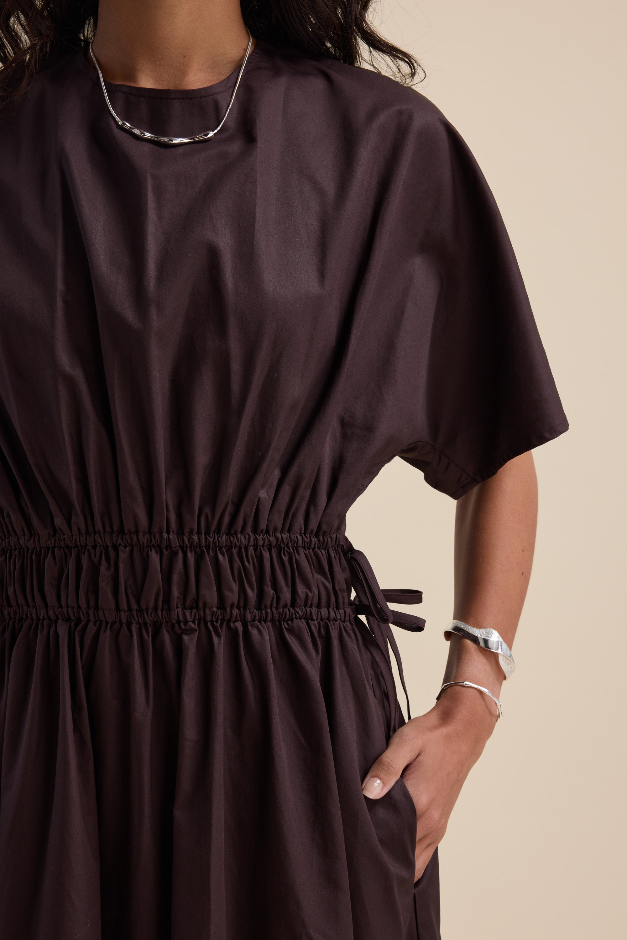 Woman in the Megan Tie Waist Dress by Max, wearing silver jewelry with hand in pocket.