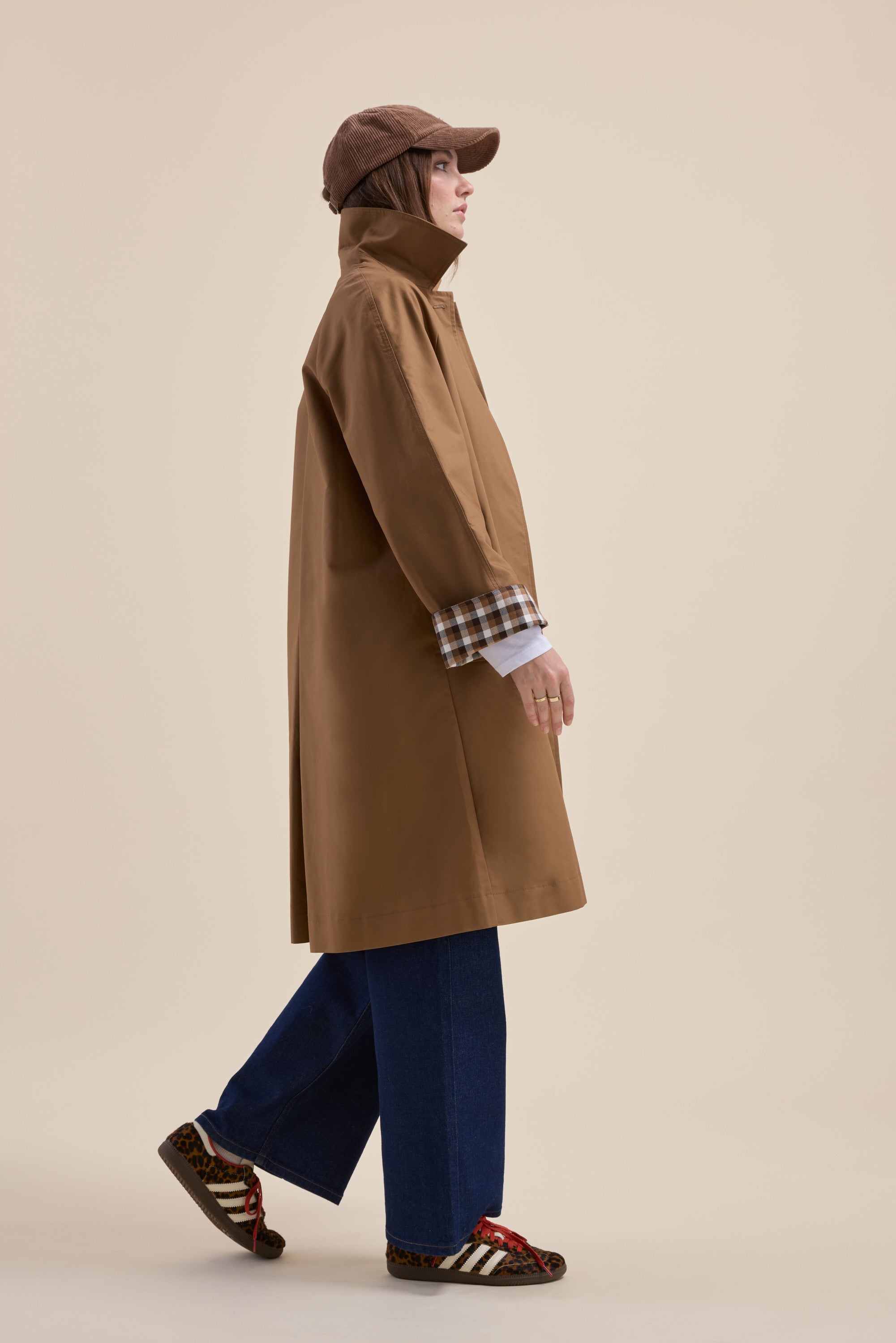 Person in a Max London Trench Coat, blue jeans, cap, and sneakers walking sideways.