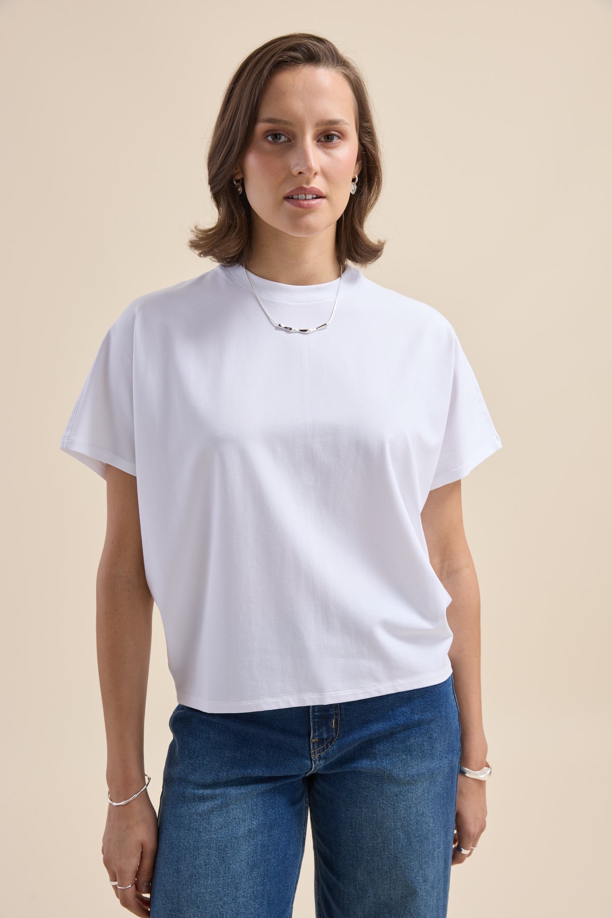 Model in Elementary Slouchy Short Sleeve Tee and blue jeans, posing by a beige background.