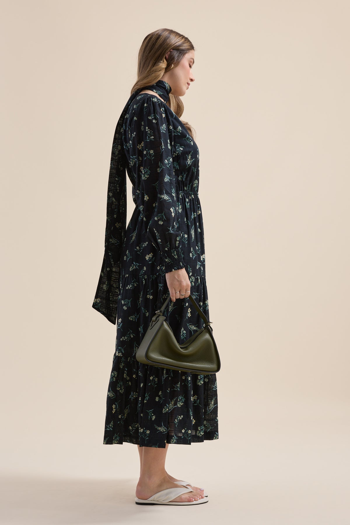Woman in Elementary Tiered Dress, holding green handbag, wearing sandals, standing sideways.