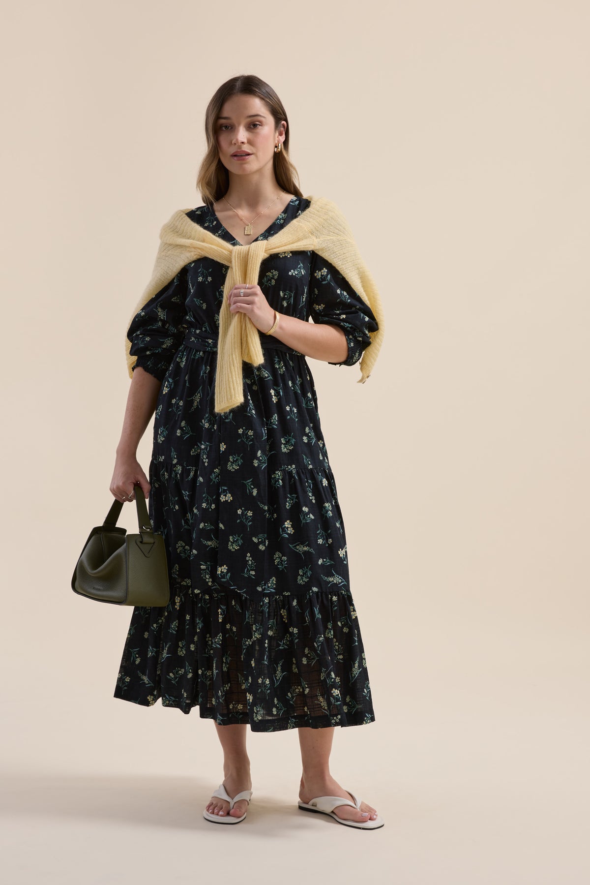Woman in an Elementary Tiered Dress, yellow sweater over shoulders, holding green handbag.