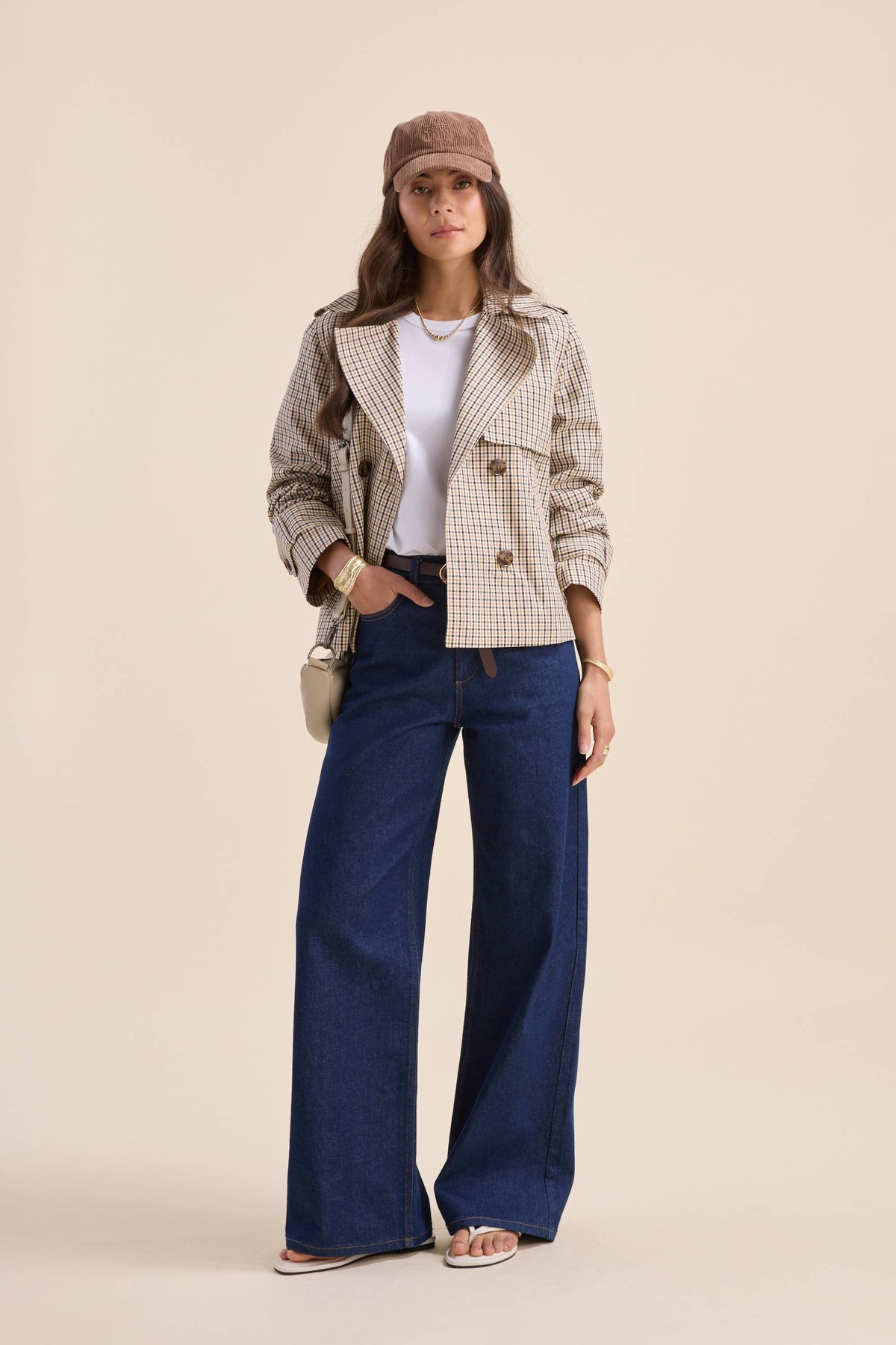 Woman in The Cropped Trench Coat by Max, wide-leg jeans, white top, cap, sandals, crossbody bag.