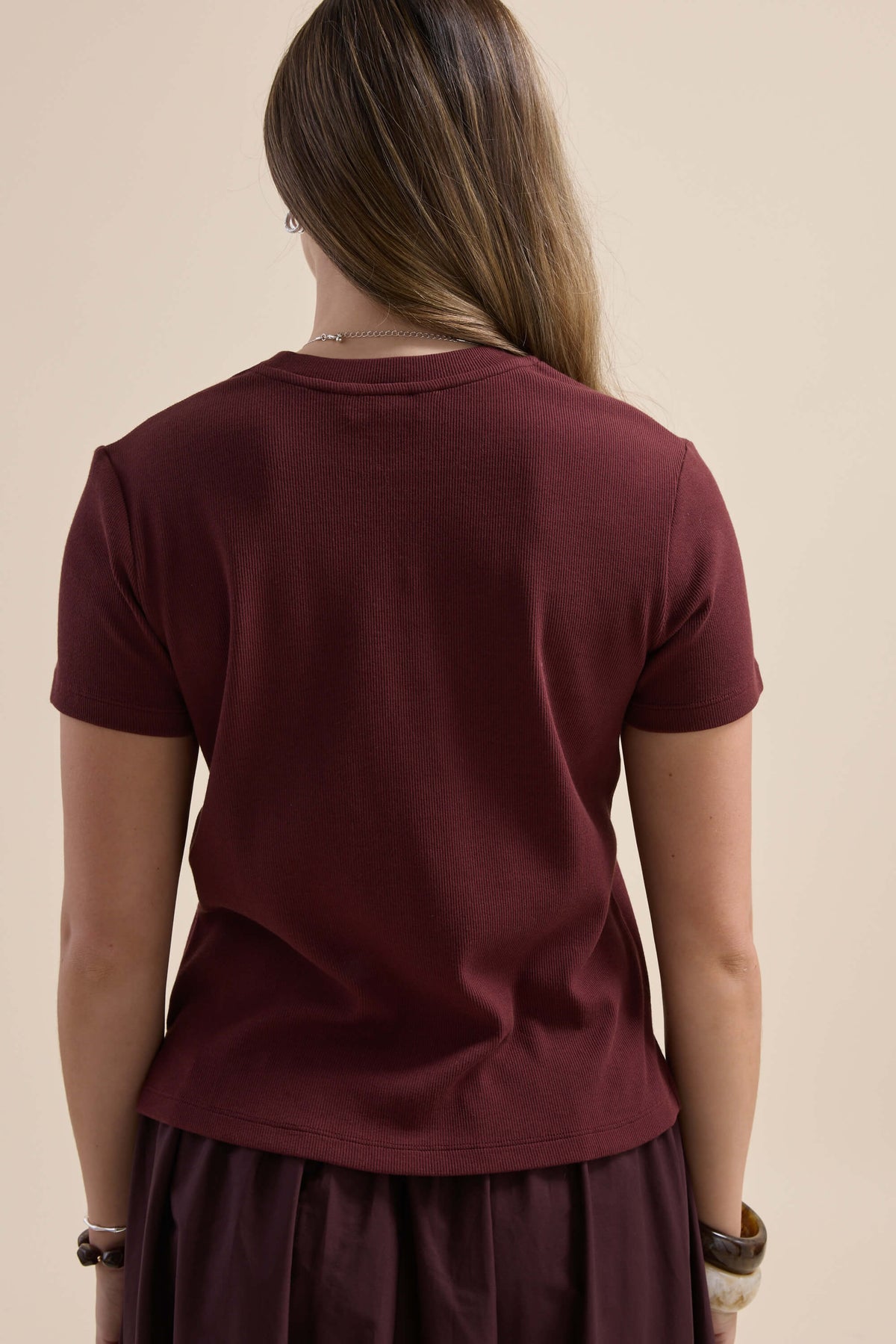 Woman in maroon Elementary Ribbed Boxy Tee with long hair, seen from behind.