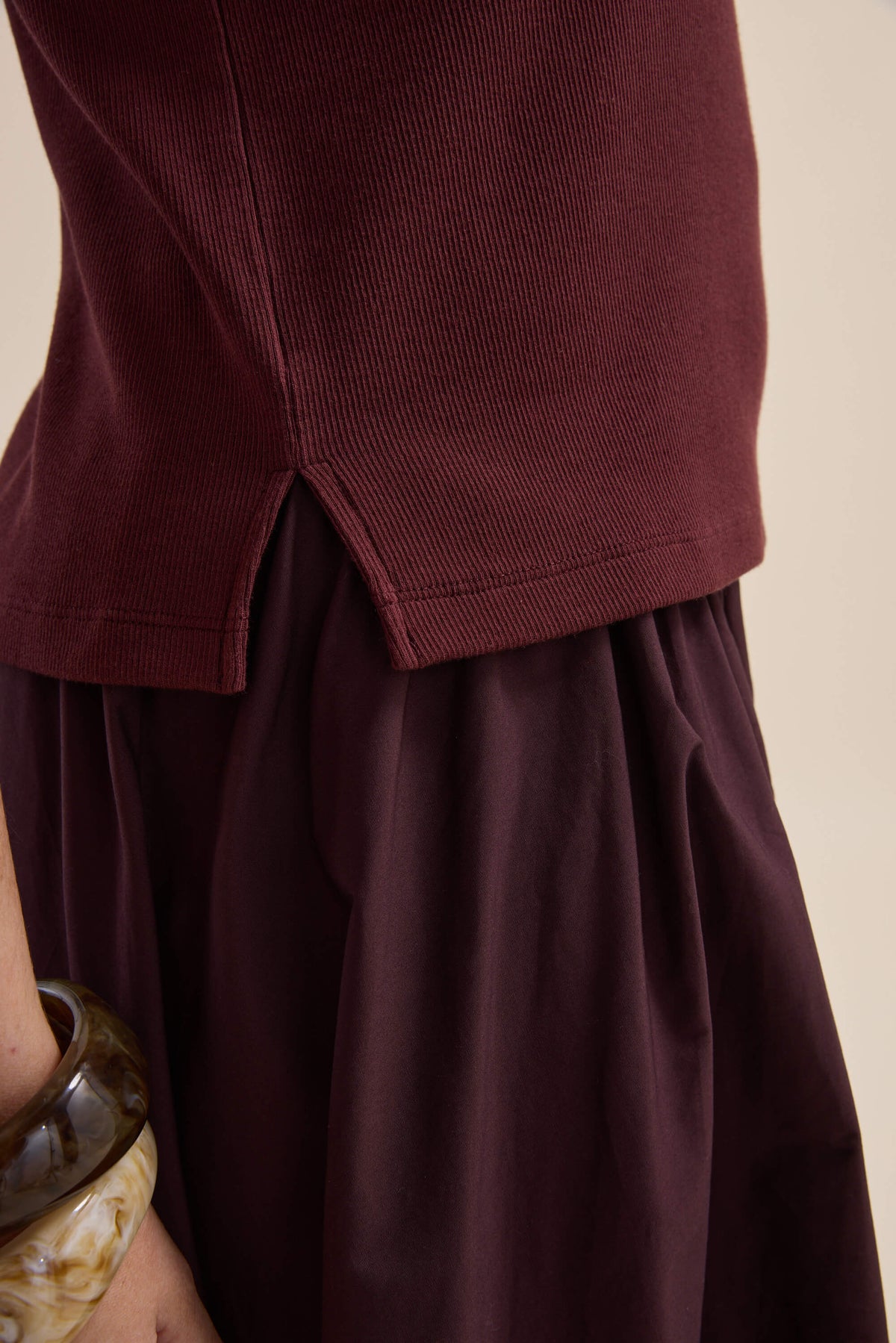 Close-up of a person in an Elementary Ribbed Boxy Tee and maroon slim fit skirt, chunky bracelet.