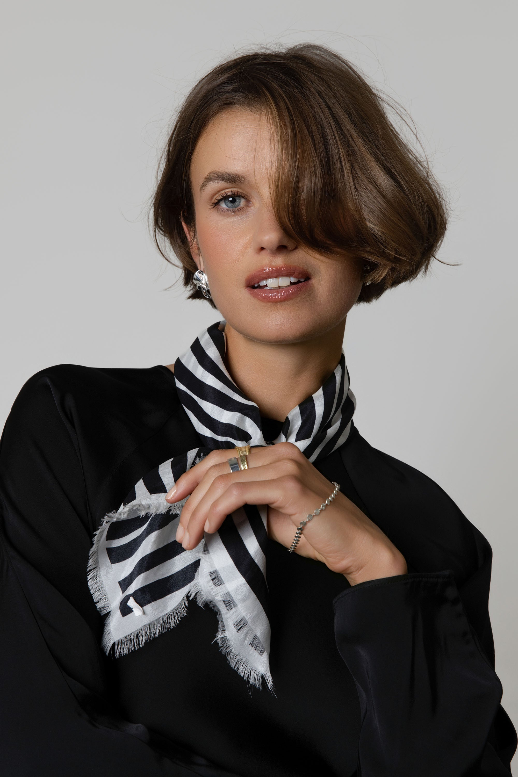 Woman with short brown hair in a Max Mable Frayed Edge Silk Scarf, black top, and jewelry.