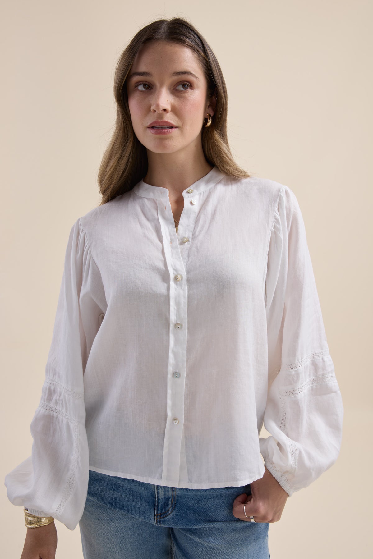 Woman in Max’s Millie Trim Detail Blouse and blue jeans stands against a beige background.