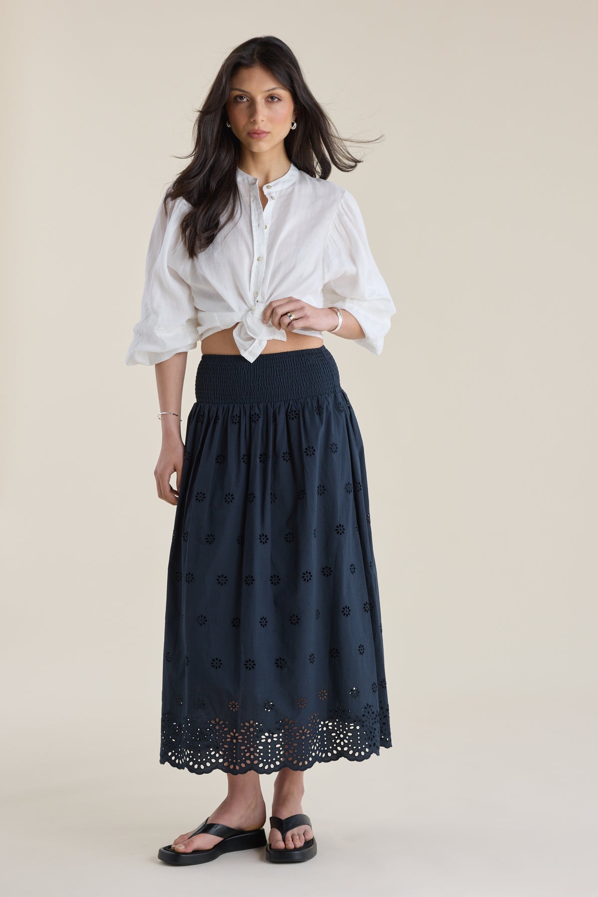 Woman in white blouse and Elementary Broderie Detail Skirt stands against plain background.