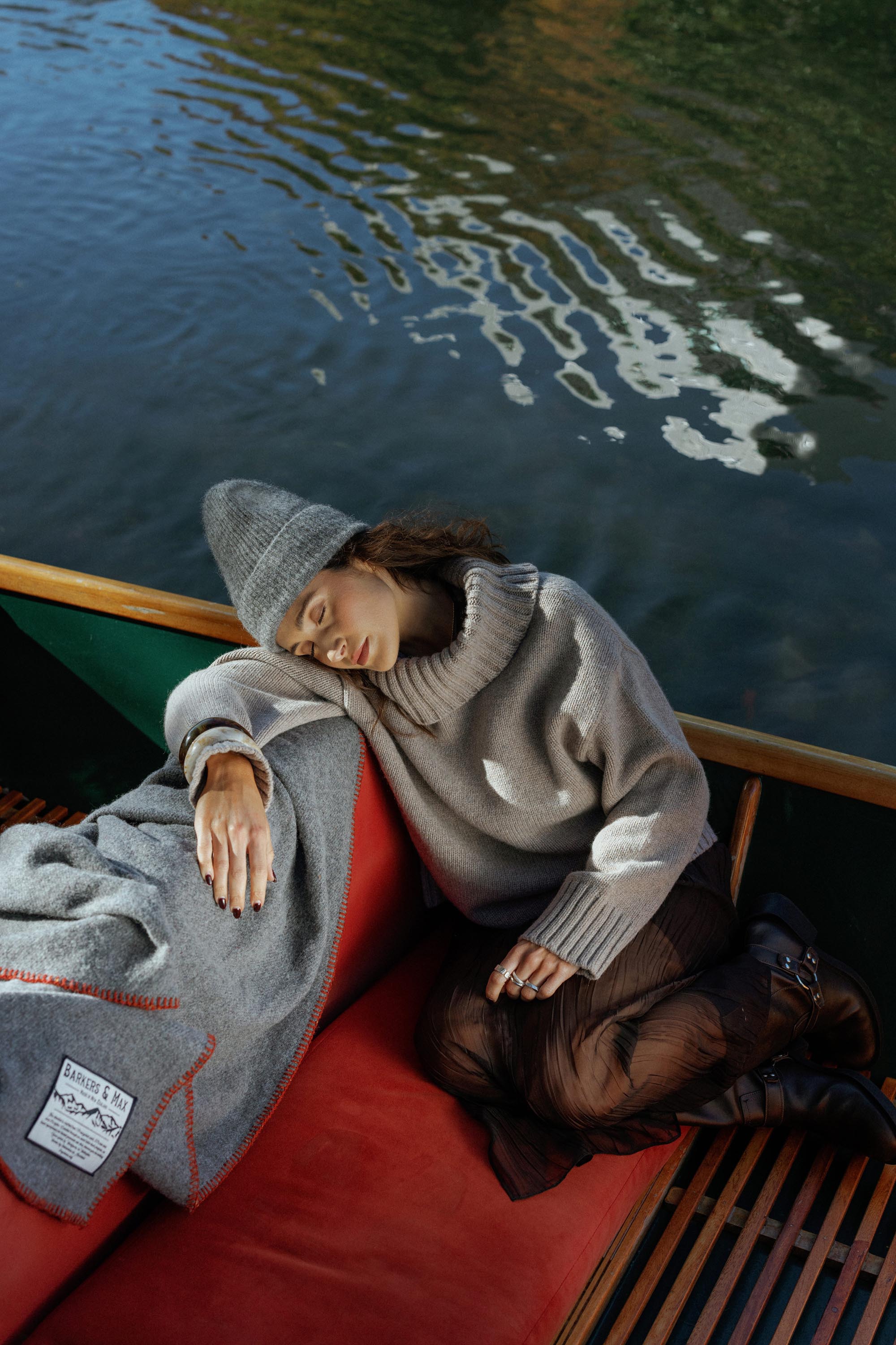 Woman naps in a Max Holly Wool Blend Roll Neck Sweater on a red boat seat beside a calm lake.