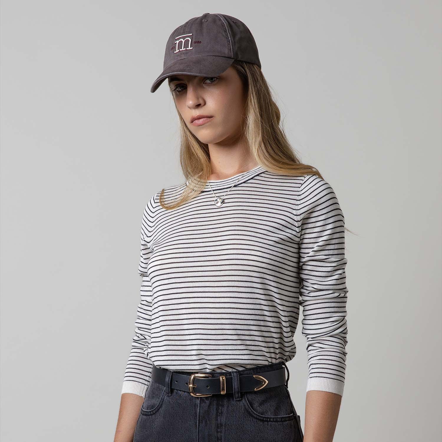 Woman in striped long-sleeve shirt and gray cap standing against a plain NZ background.