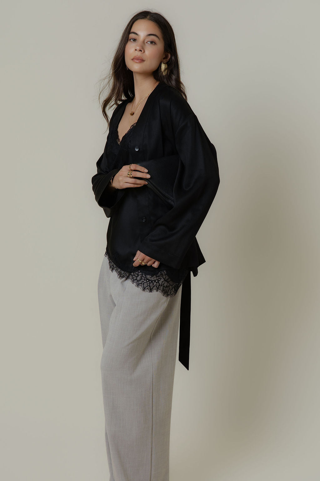 Woman wears Max’s The Tie Waist Top and gray wide-leg pants against a plain light background.