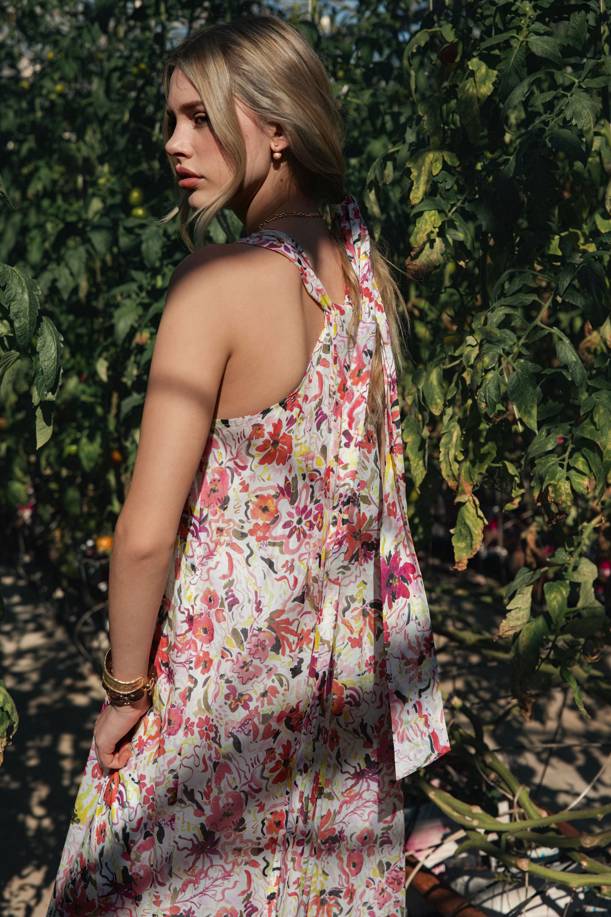 A woman standing in a greenhouse wearing a floral spring dress.