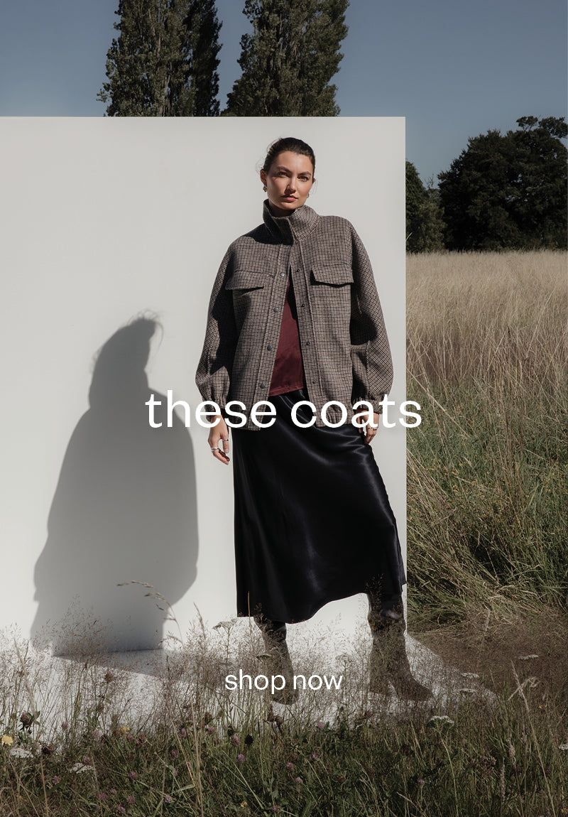 Woman modeling a plaid coat and black skirt outdoors in NZ. These coats, shop now.