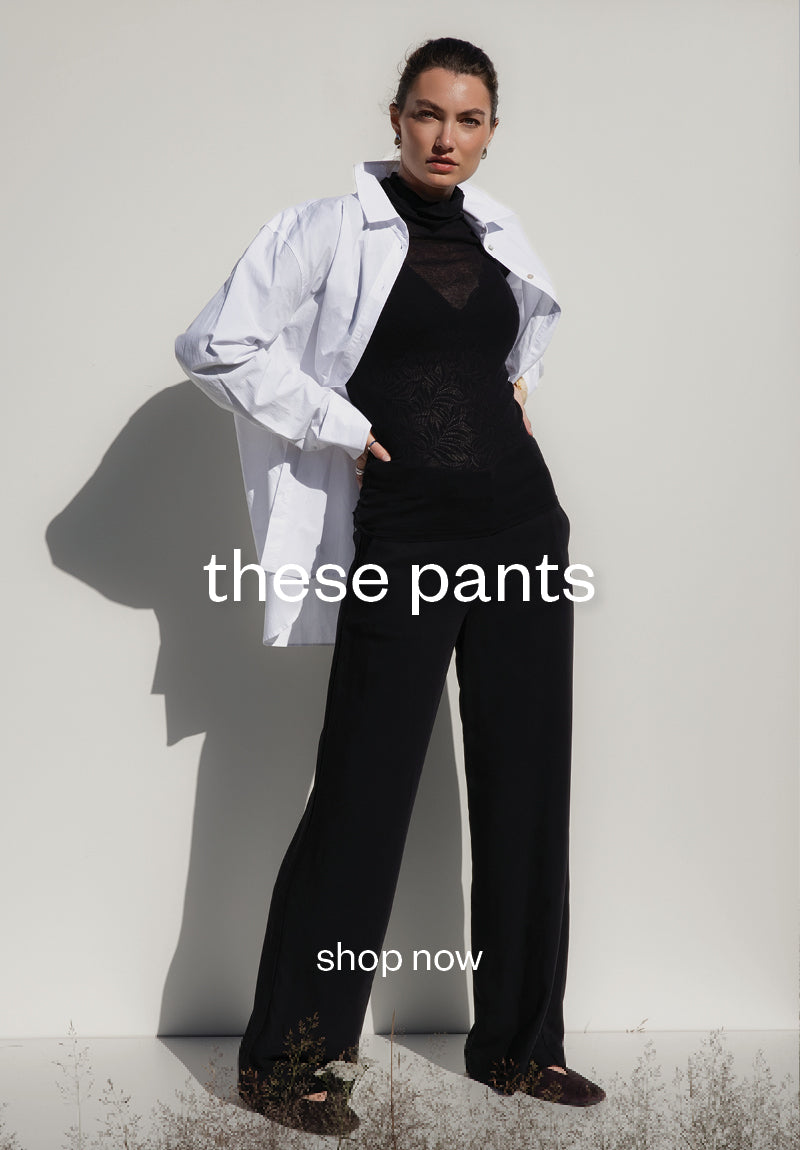 Woman in black pants and white shirt stands against a light NZ background; text reads these pants.