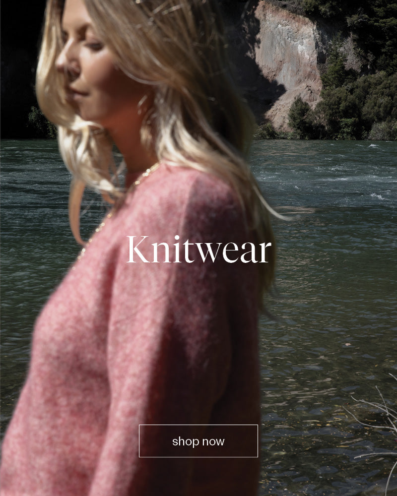 Woman in a pink sweater by a NZ river with Knitwear and shop now text overlaid.