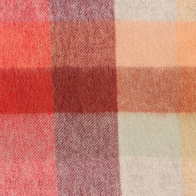 Close-up of a soft, NZ-inspired plaid fabric with red, beige, orange, and pink squares and stripes.
